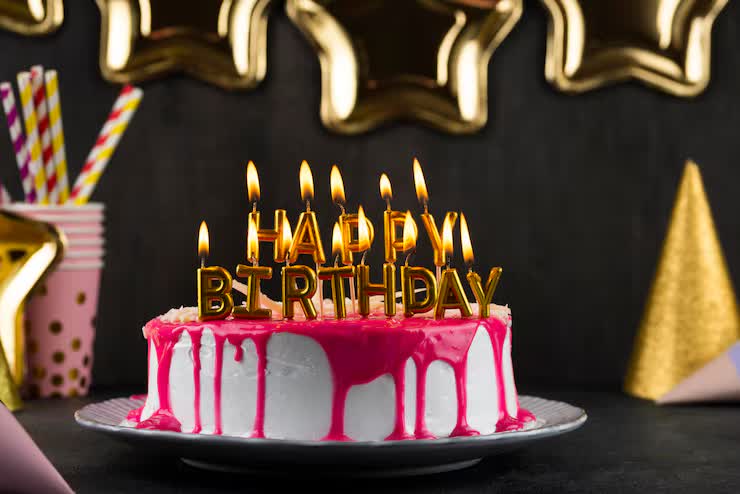 Pink and white birthday cake with lit Happy Birthday candles